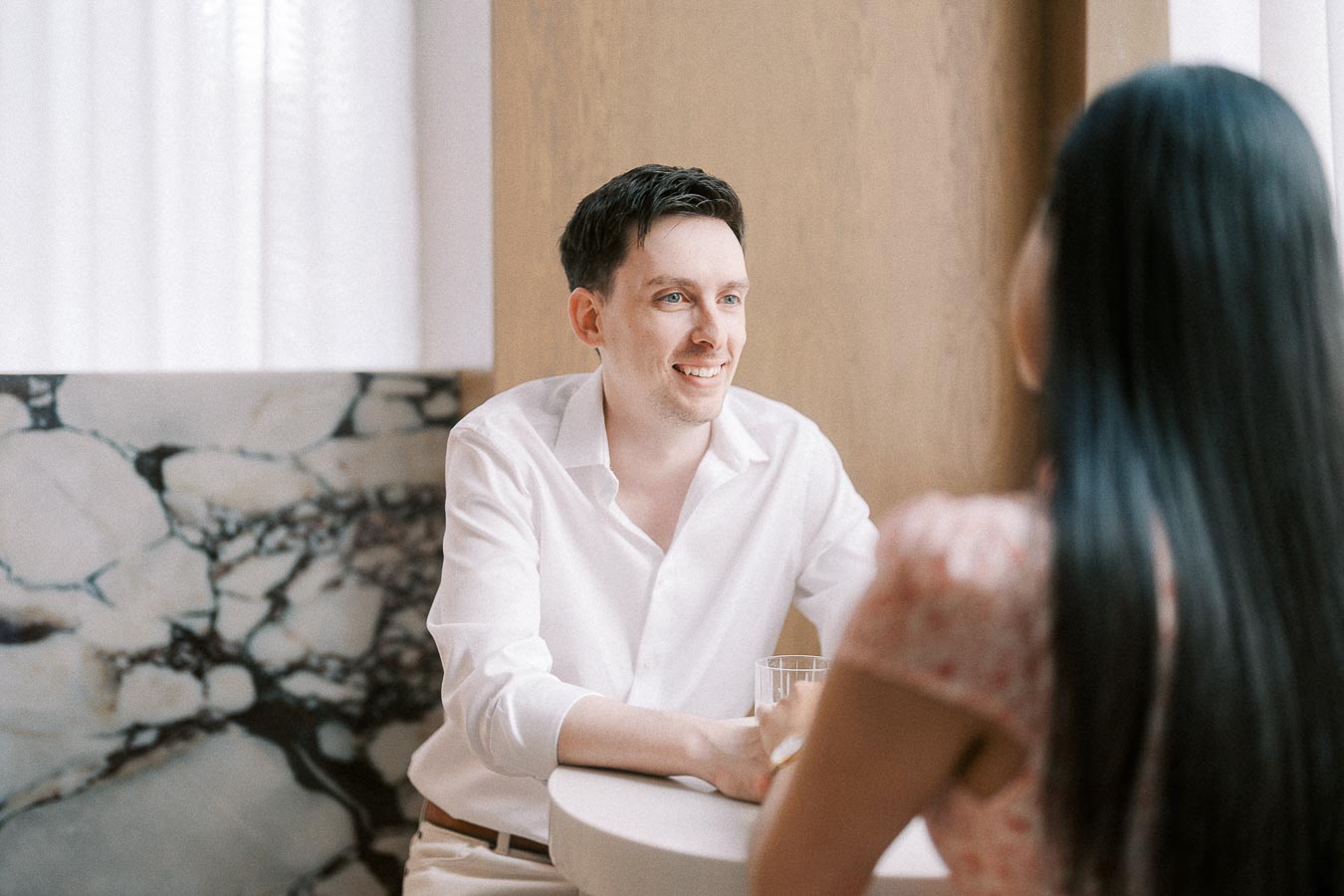 Man in white shirt smiling at his partner across a small café table