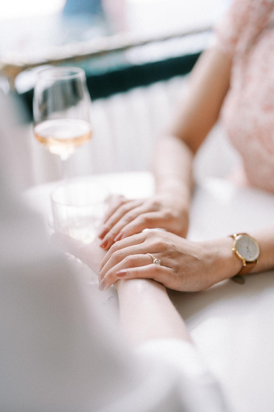 Close-up of Becky’s engagement ring as she holds Mike’s hand beside a wine glass