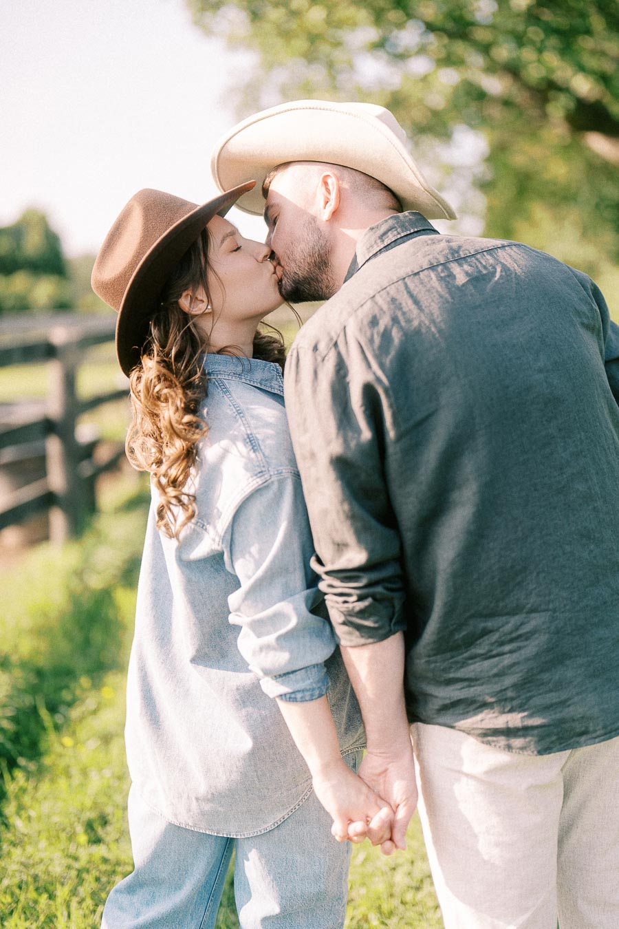 Expectant couple in cowboy hats kissing beside a farm fence in Flamborough