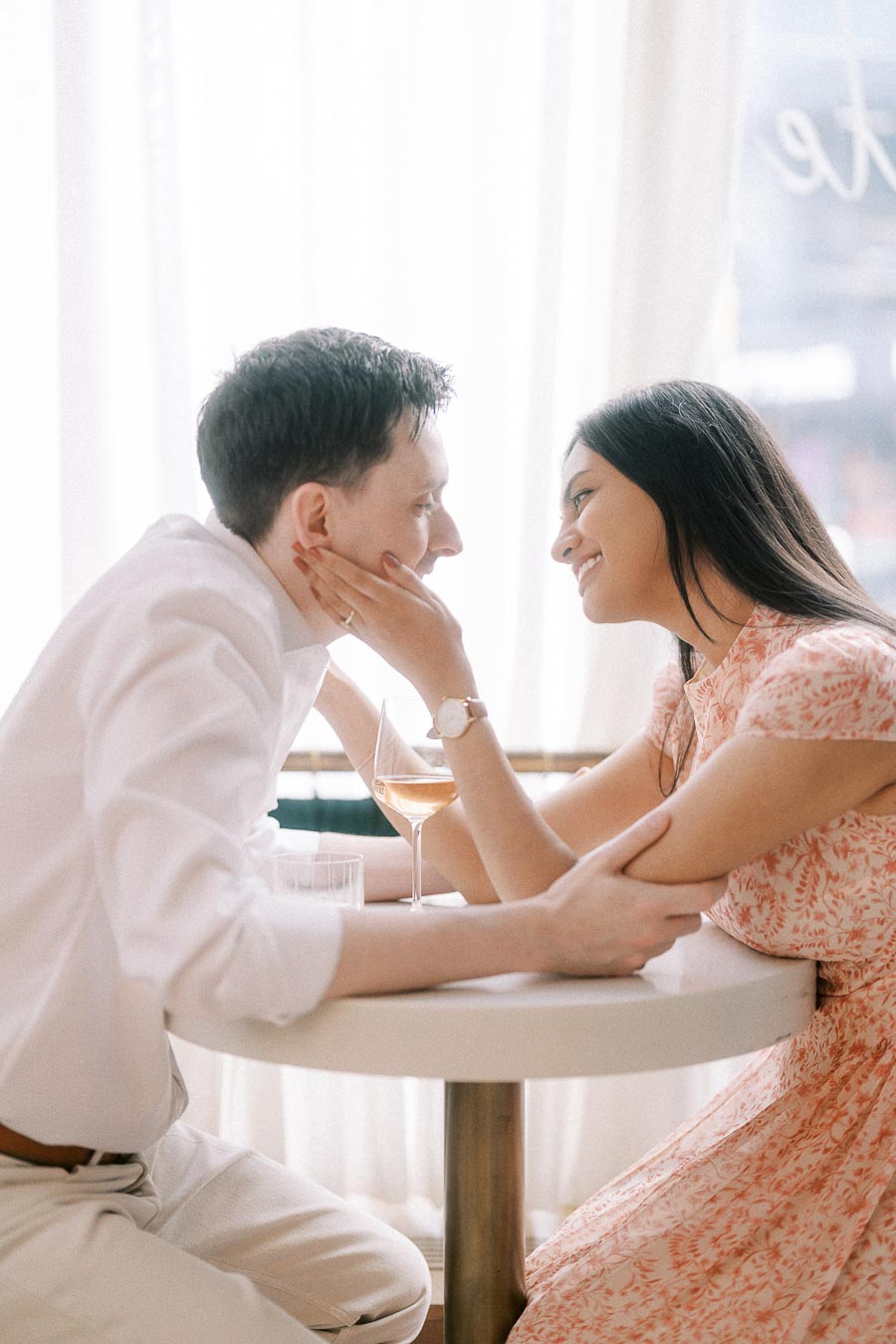 Couple smiling across a small café table with drinks in soft window light