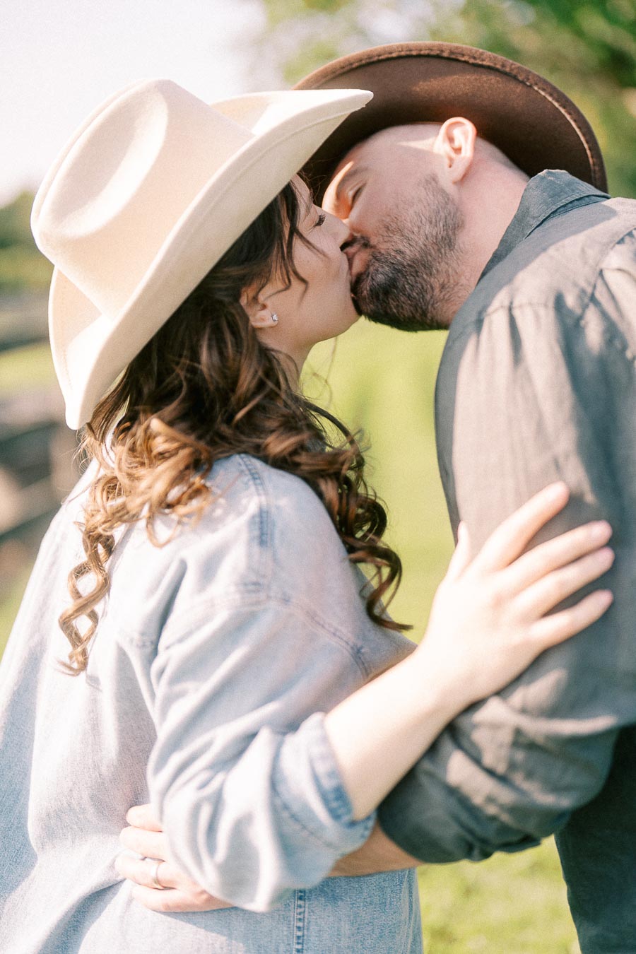 Expectant couple in cowboy hats kissing outdoors at The Green Acres