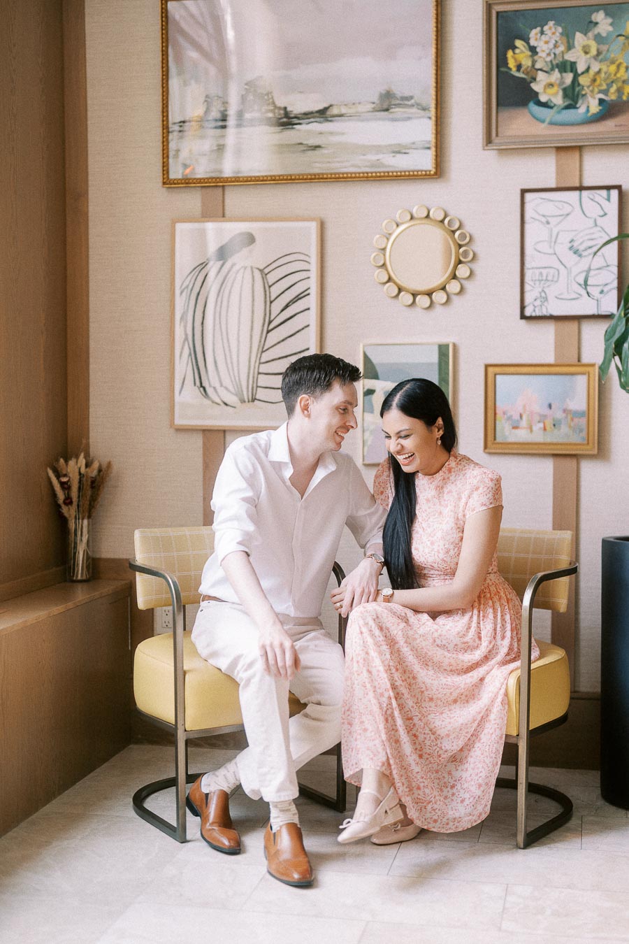 Couple seated together on yellow chairs beneath a gallery wall of framed art