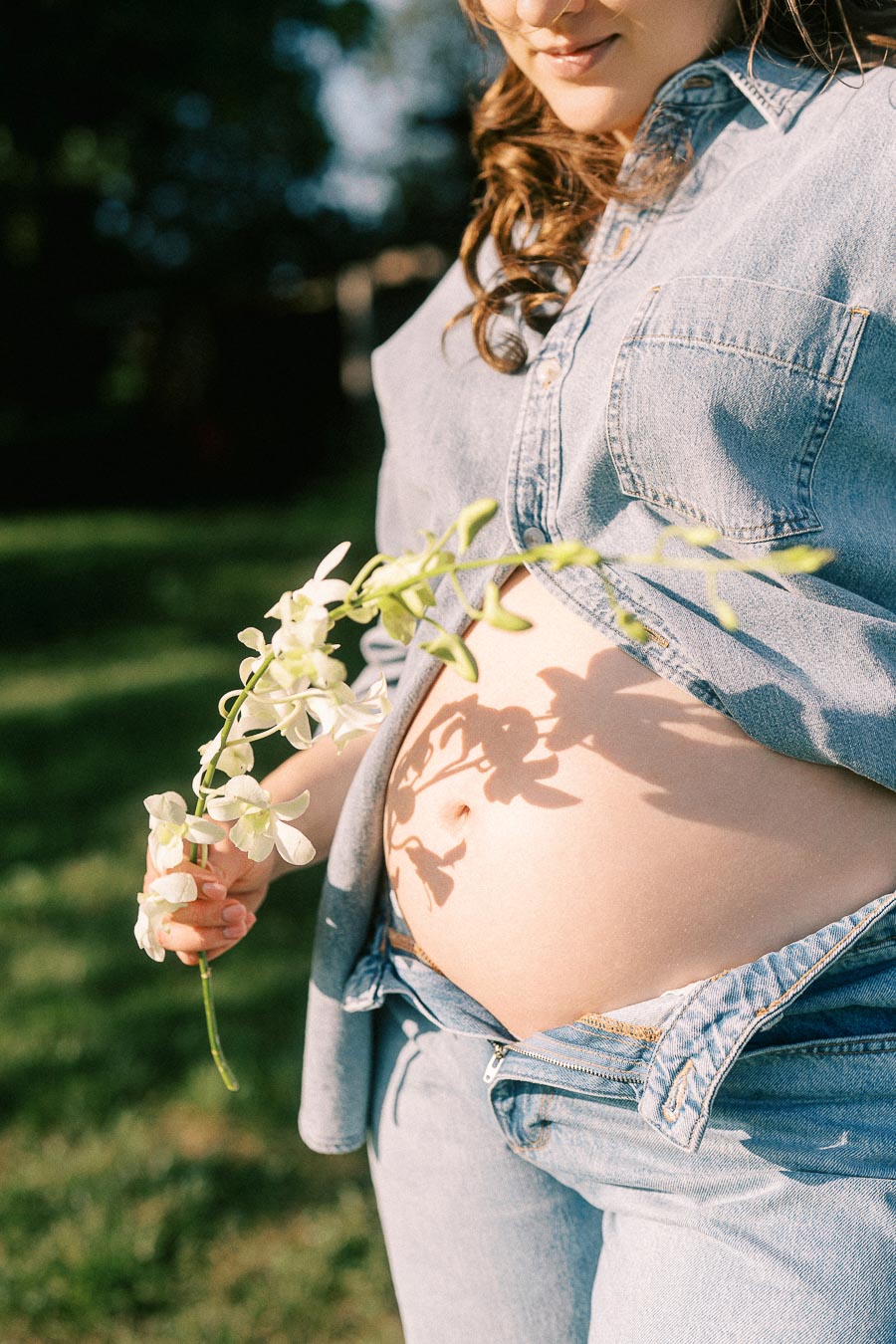 Pregnant woman in denim holding white flowers at The Green Acres