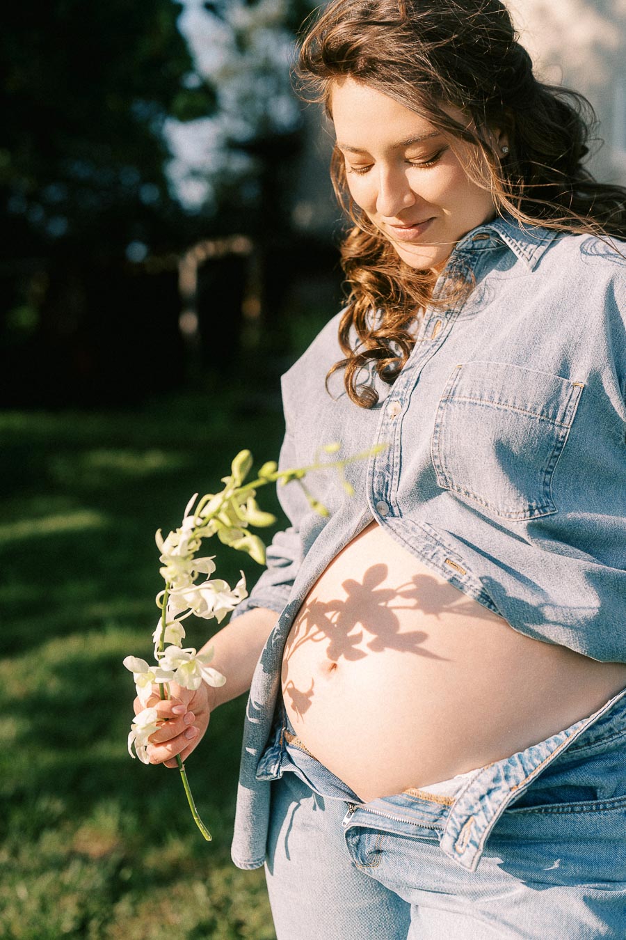 Pregnant woman in denim holding white flowers at The Green Acres