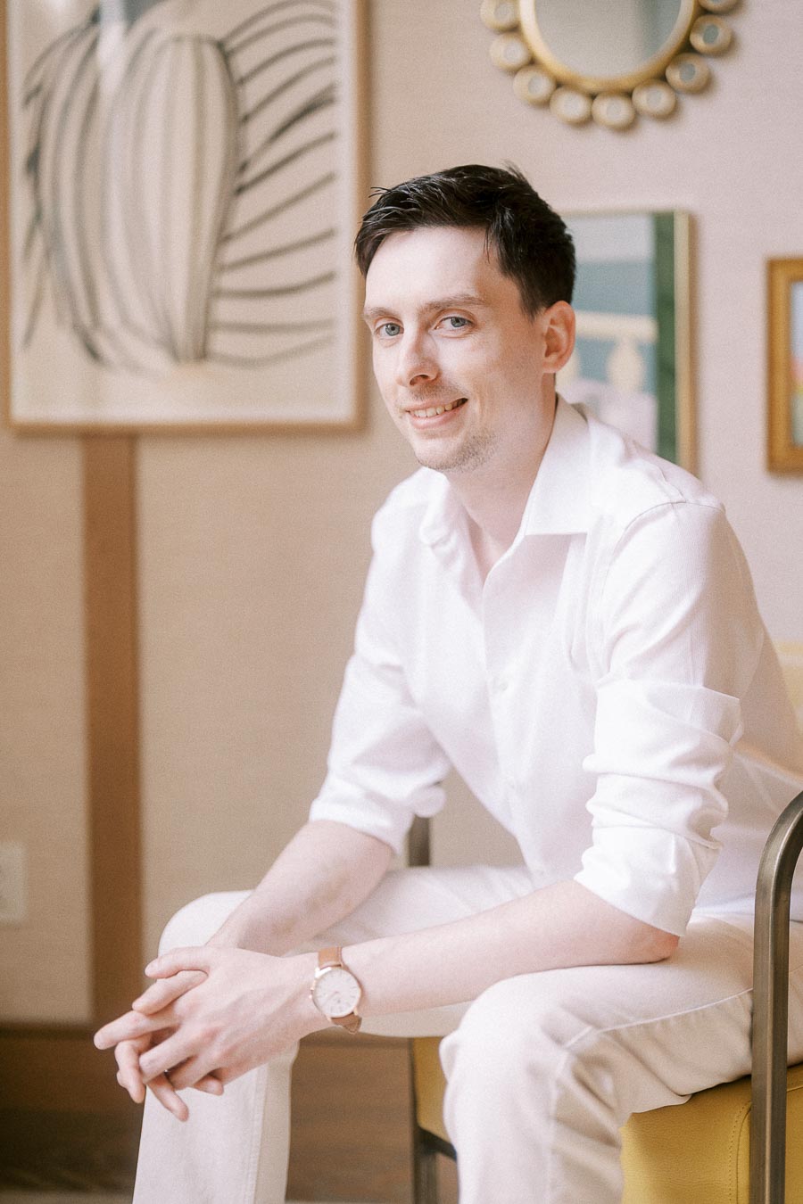 Mike seated in a white outfit in a softly decorated Toronto interior