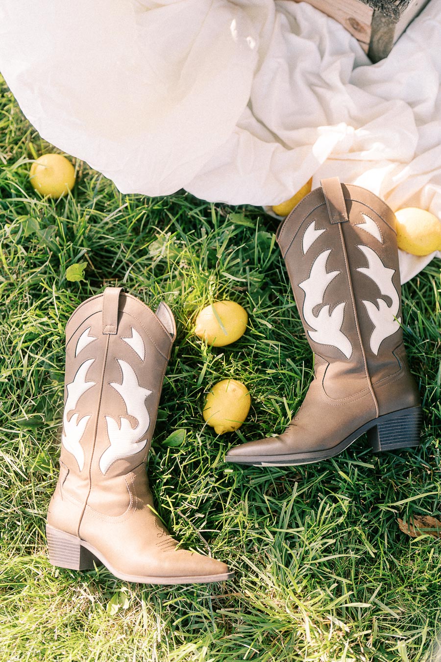 Western boots and yellow apples on grass beside white fabric