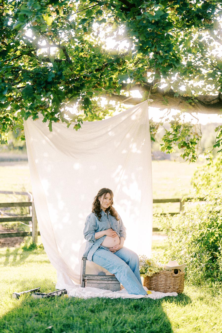 Pregnant woman seated under a tree with white fabric backdrop at The Green Acres