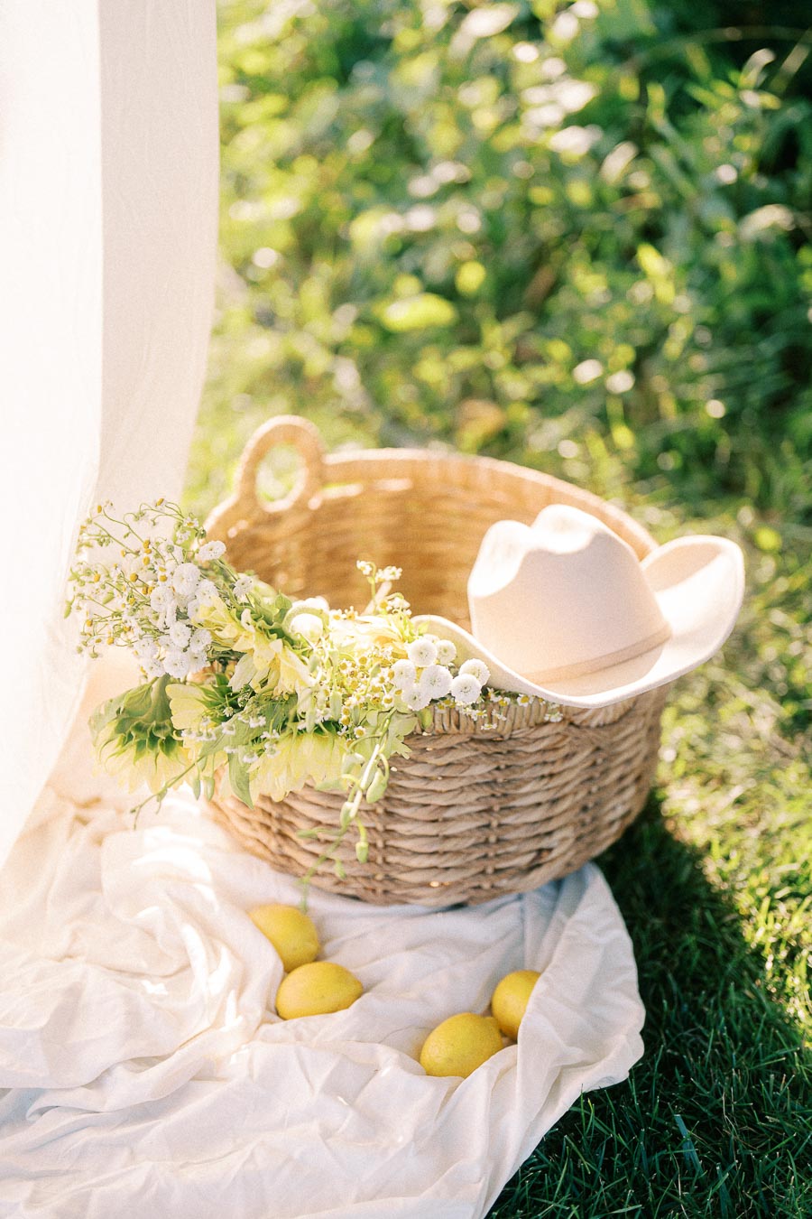 Wicker basket with flowers, cowboy hat, and lemons on a white blanket