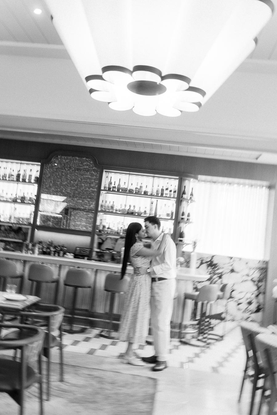 Couple embracing in a stylish Toronto bar beneath a large floral light fixture