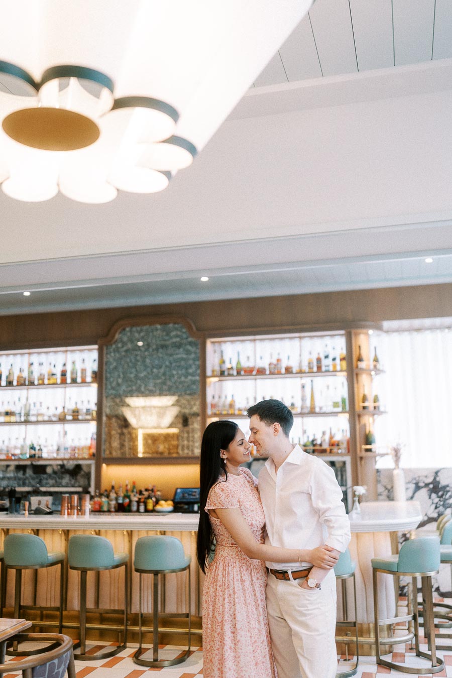 Couple embracing in a stylish Toronto hotel bar with pastel stools and backlit shelves