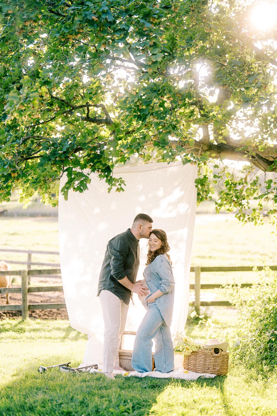 Expectant couple posing under a leafy tree at The Green Acres