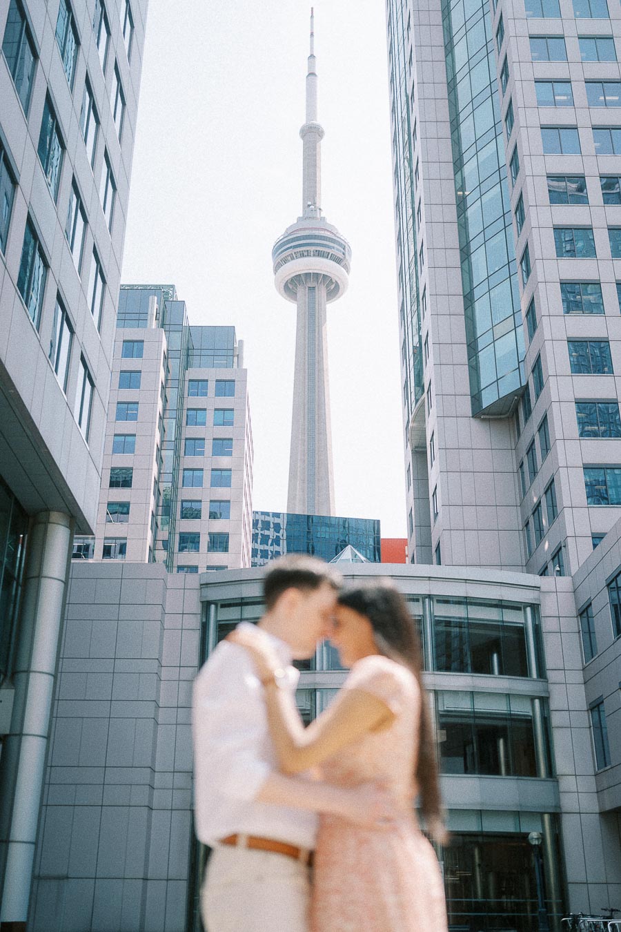 Couple kissing beneath the CN Tower between downtown Toronto buildings