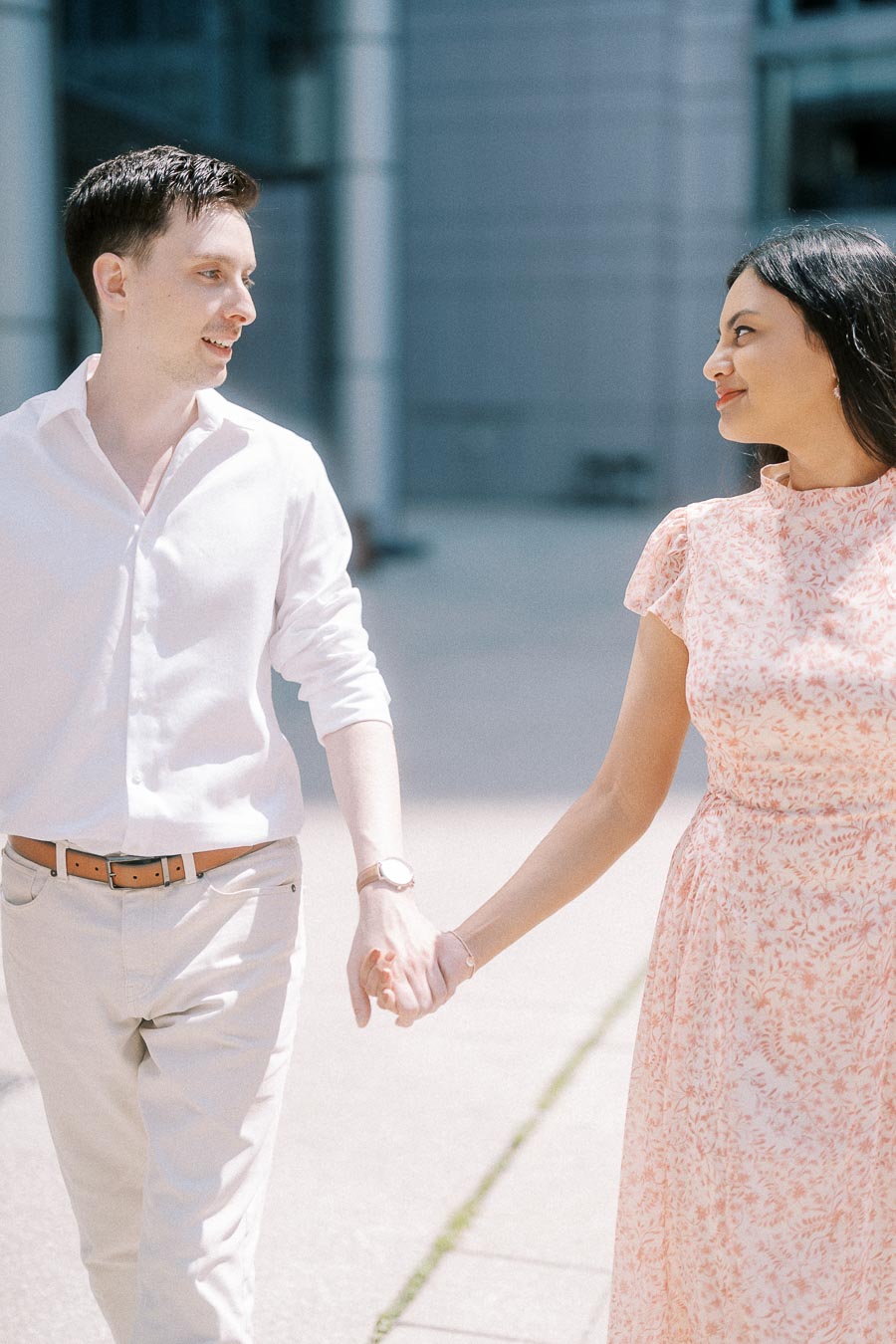 Couple holding hands and smiling at each other on a sunny Toronto sidewalk