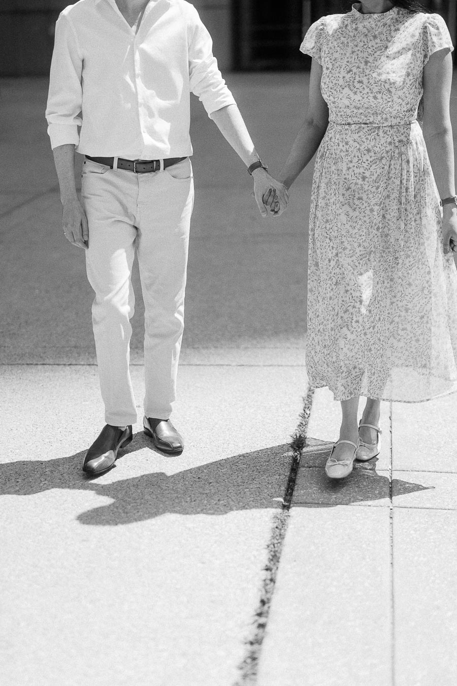 Couple holding hands while walking on a sunlit Toronto sidewalk in black and white