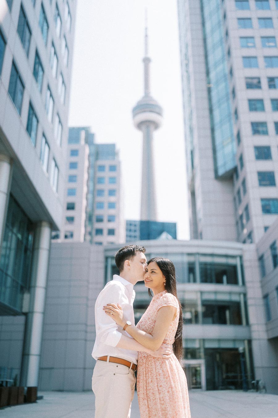 Engaged couple embracing in downtown Toronto with the CN Tower behind them