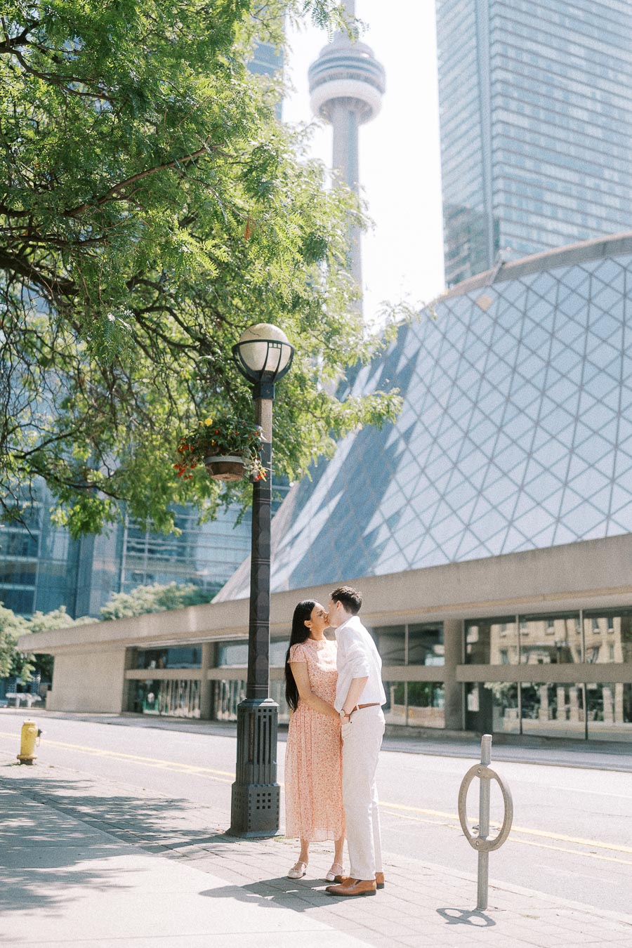 Couple kissing on a Toronto sidewalk with CN Tower and Roy Thomson Hall behind them