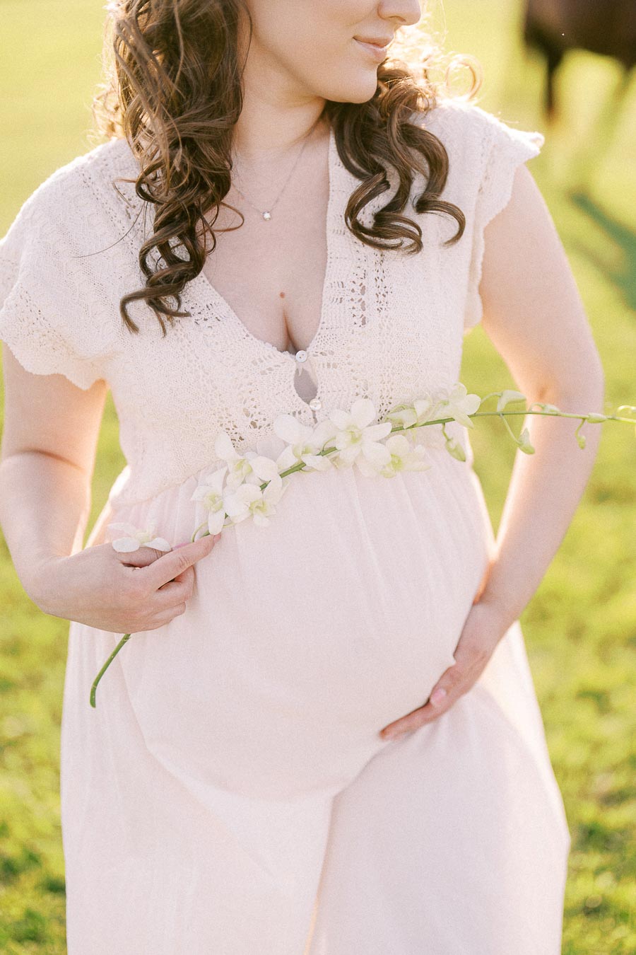 Expectant mother holding white flowers in a sunlit field at The Green Acres