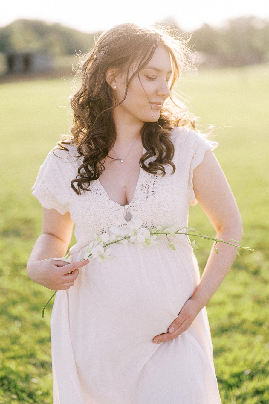 Expectant mother in a white dress holding flowers in a sunlit field