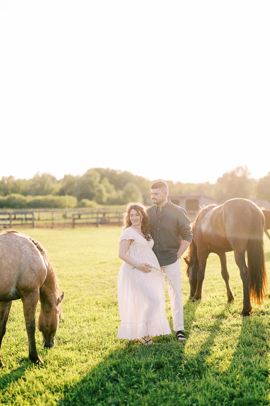 Expectant couple standing in a grassy horse pasture at The Green Acres