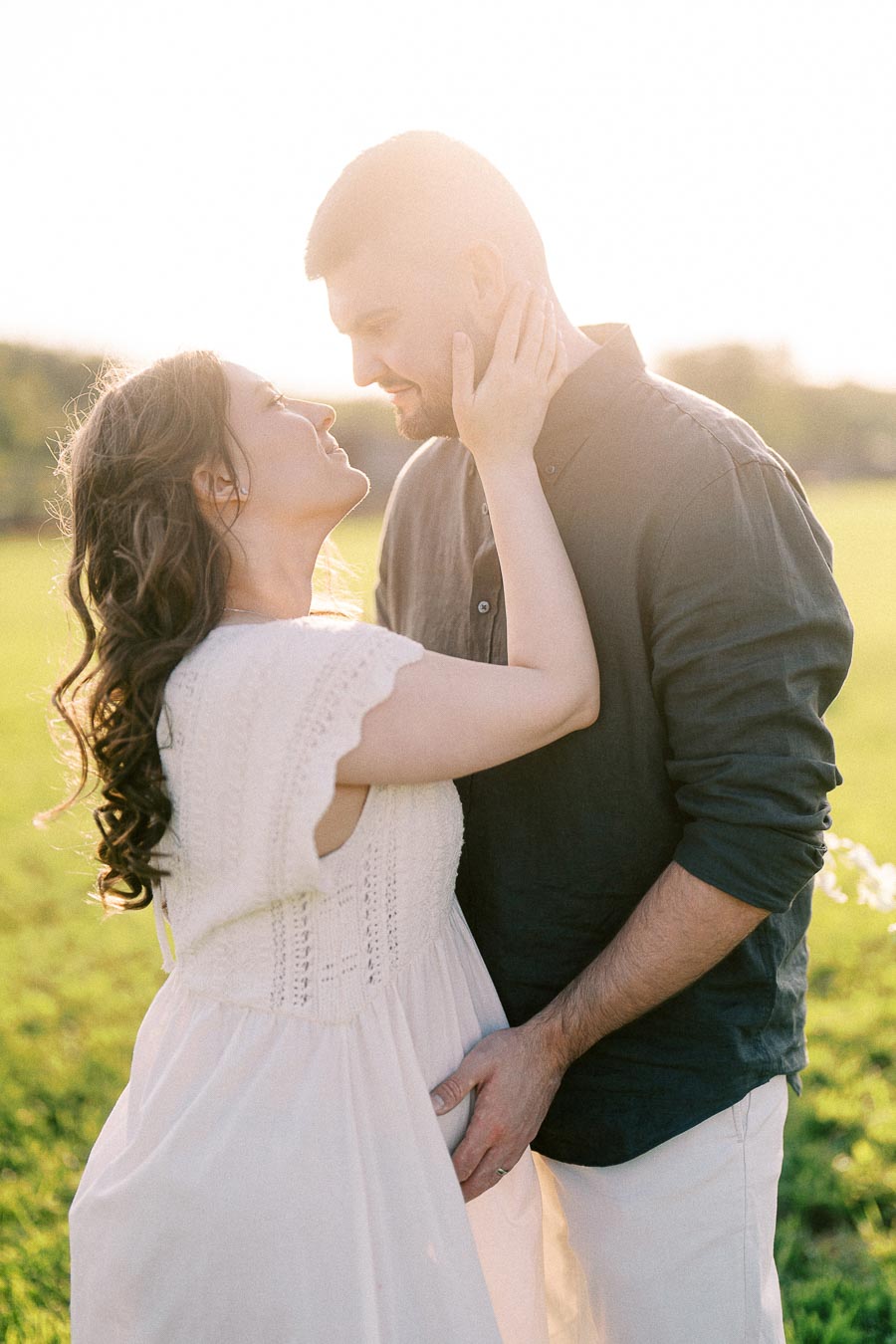 Expectant couple embracing in a sunlit field at The Green Acres