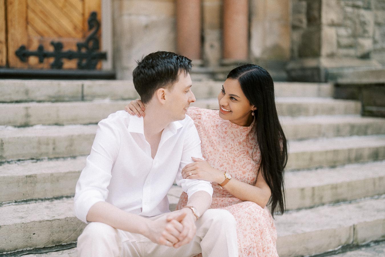 Couple sitting close on stone steps, smiling at each other