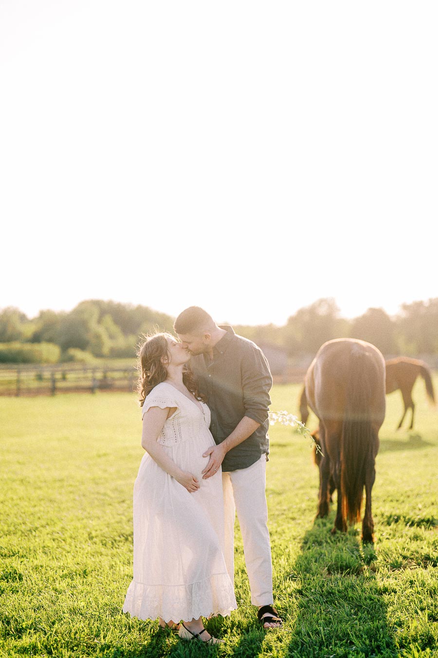 Expectant couple kissing in a grassy horse pasture at The Green Acres