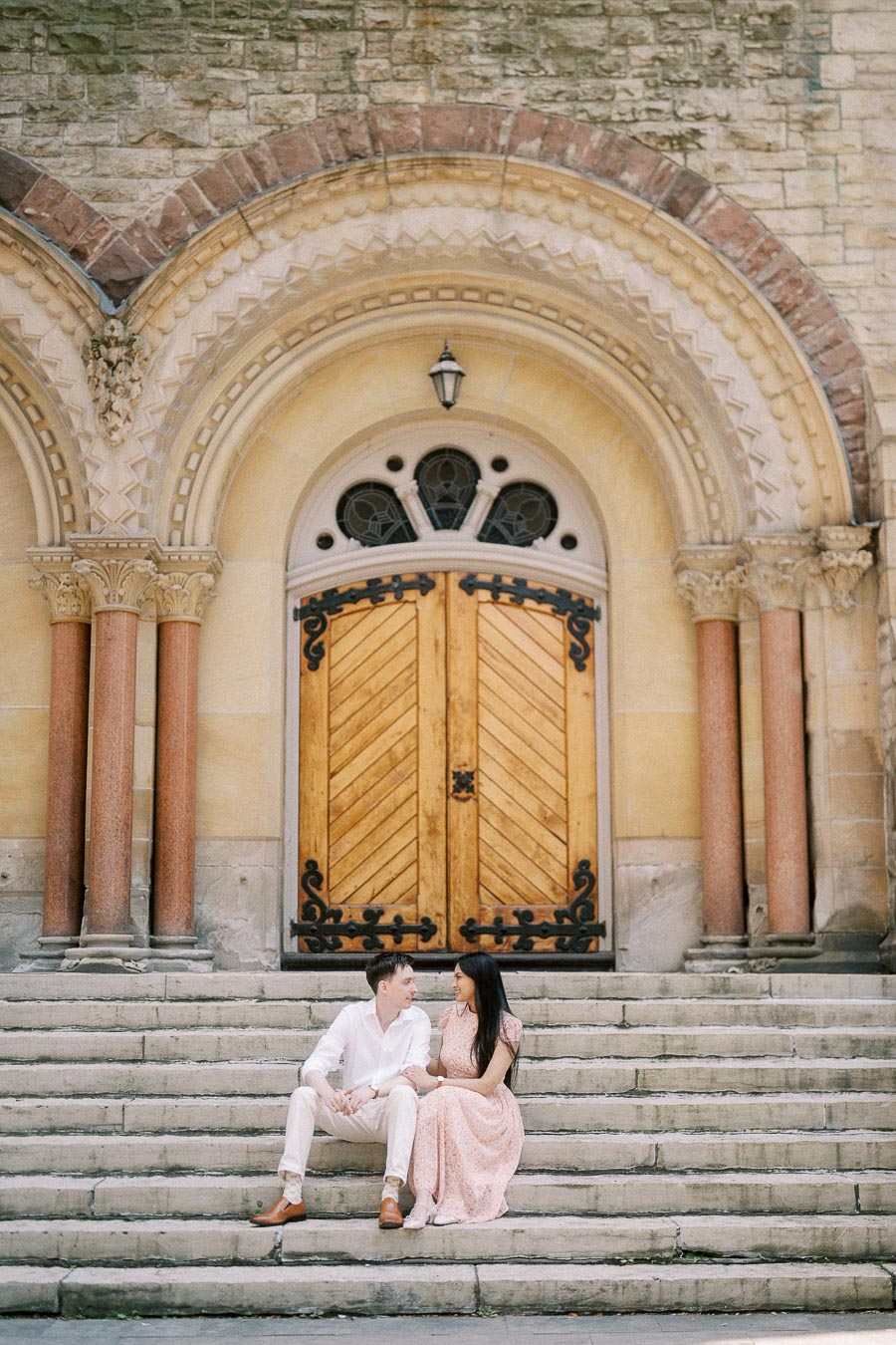 Couple seated on stone steps beneath an ornate arched wooden doorway in Toronto