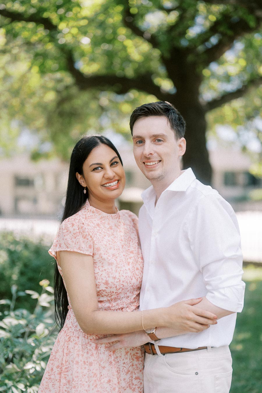 Smiling couple embracing under leafy trees during a Toronto engagement session