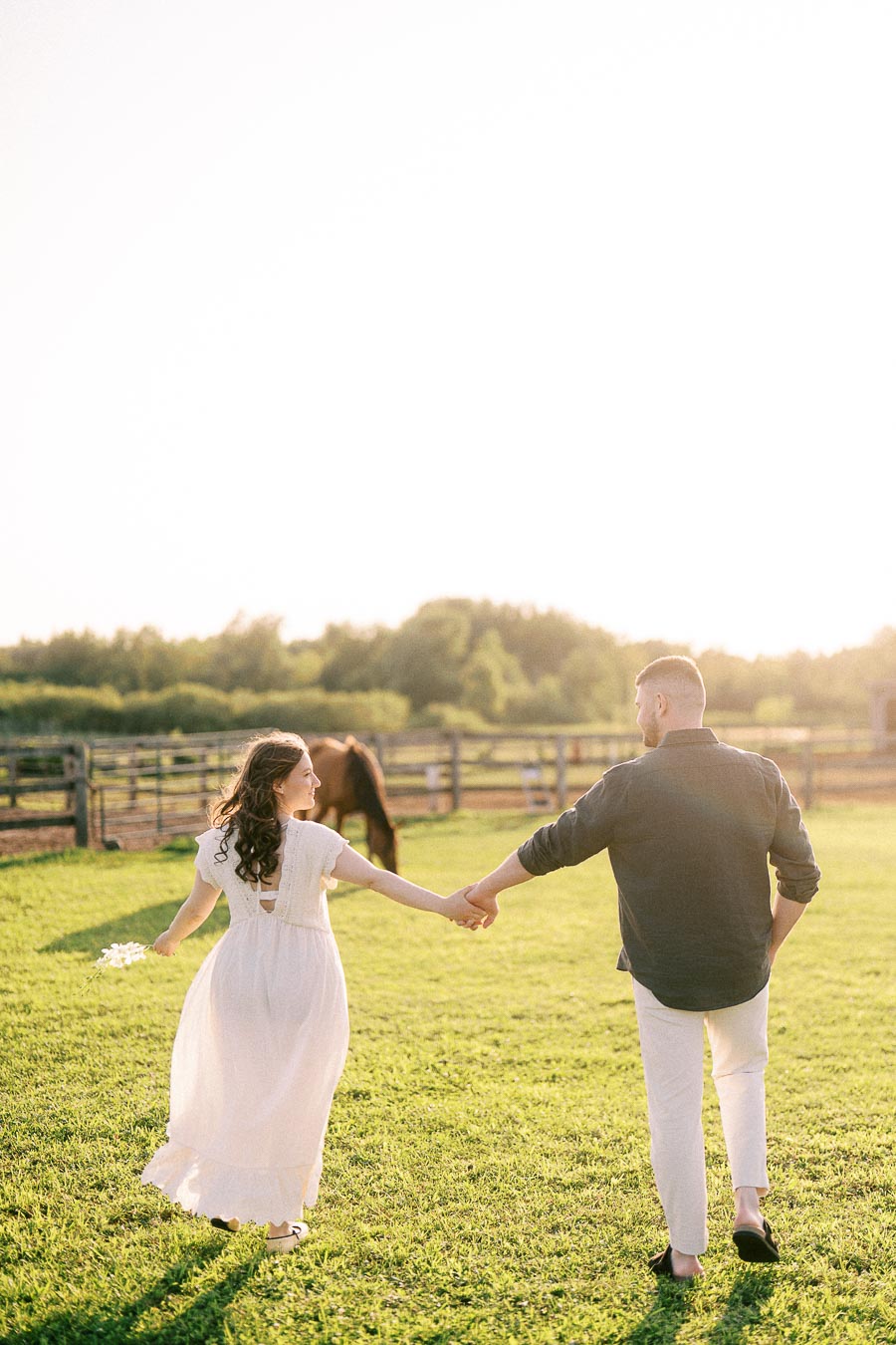 Expectant couple holding hands in a pasture at The Green Acres