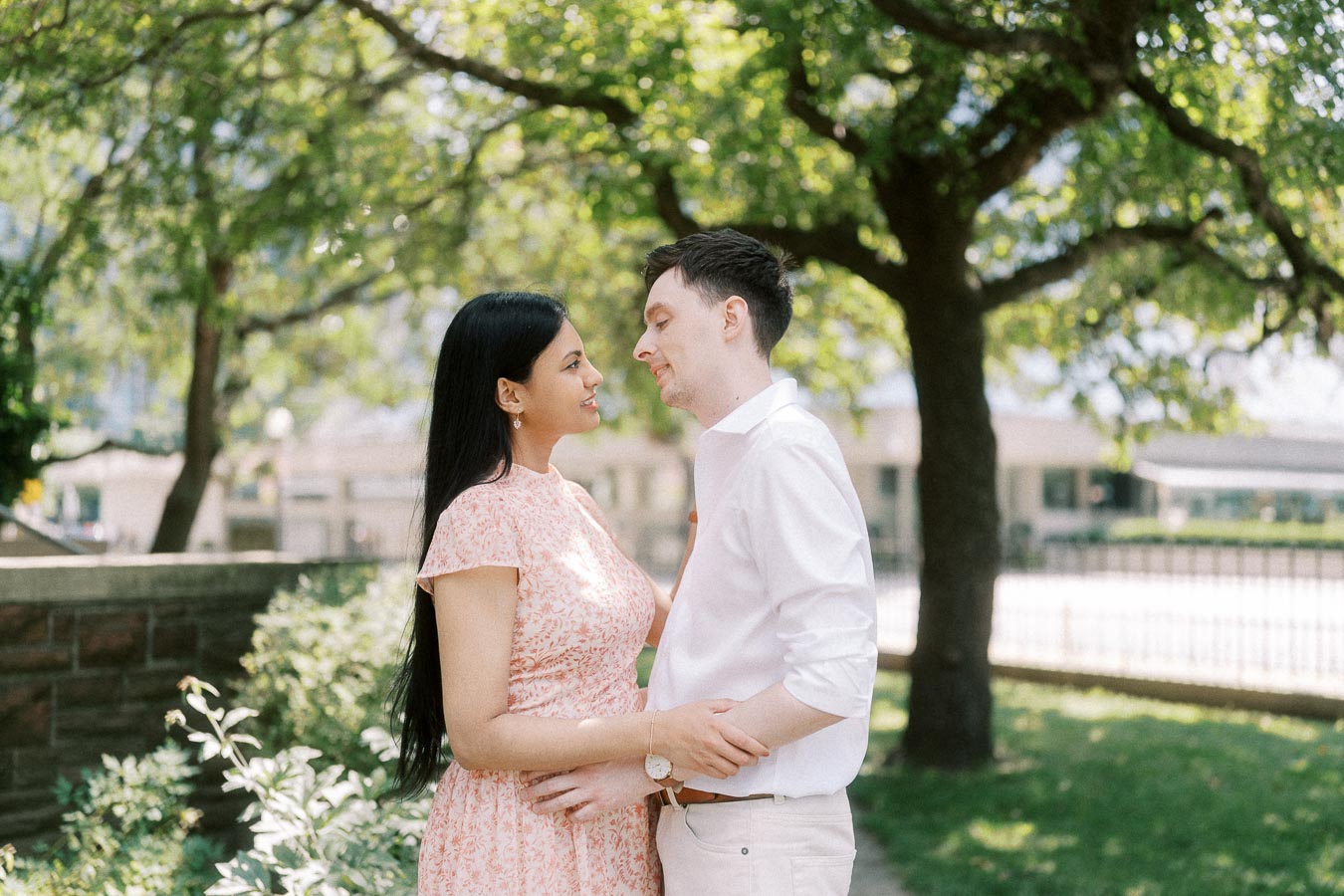 Couple standing close beneath leafy trees in a sunlit Toronto garden
