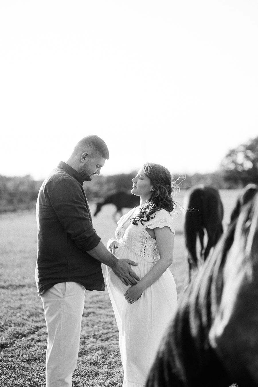 Expectant couple in a pasture with horses at The Green Acres