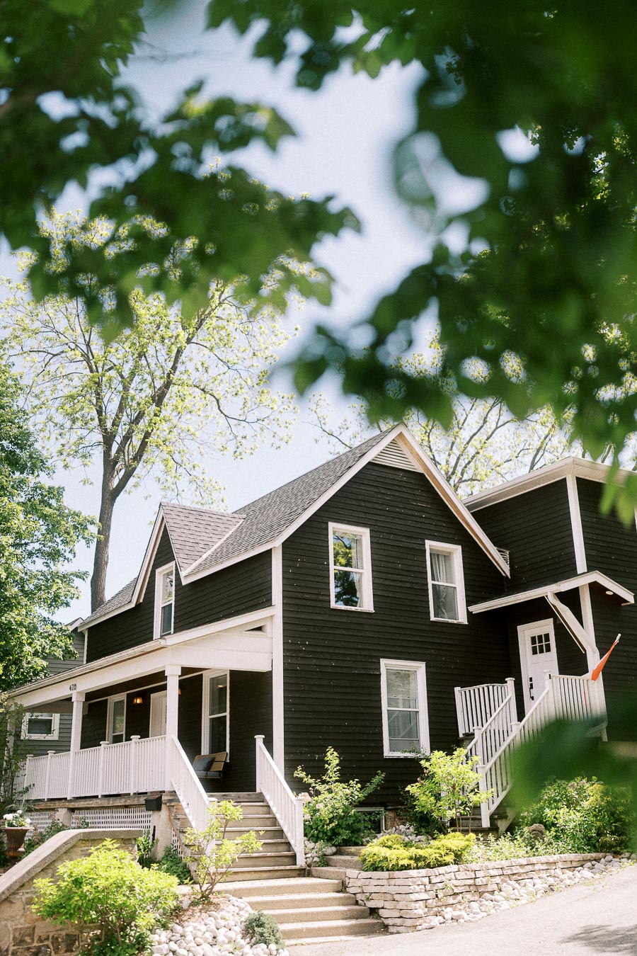 Black and white historic building with porch and steps framed by green leaves at Ancaster Mill.