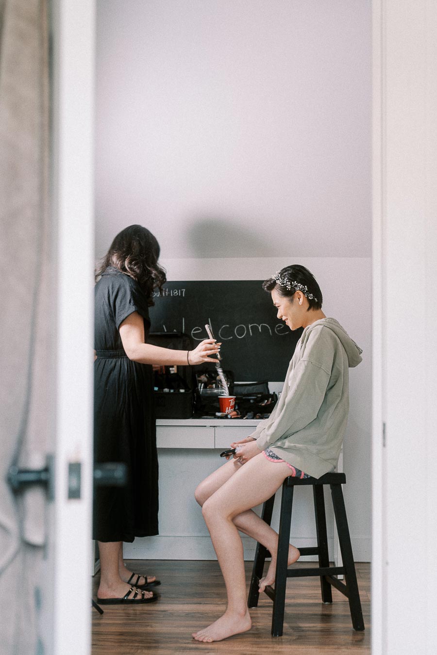 Bride seated on a stool while a stylist works on her hair during wedding morning preparations