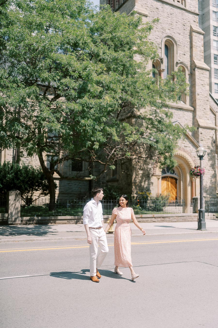 Couple walking hand in hand on a Toronto street beside a stone church