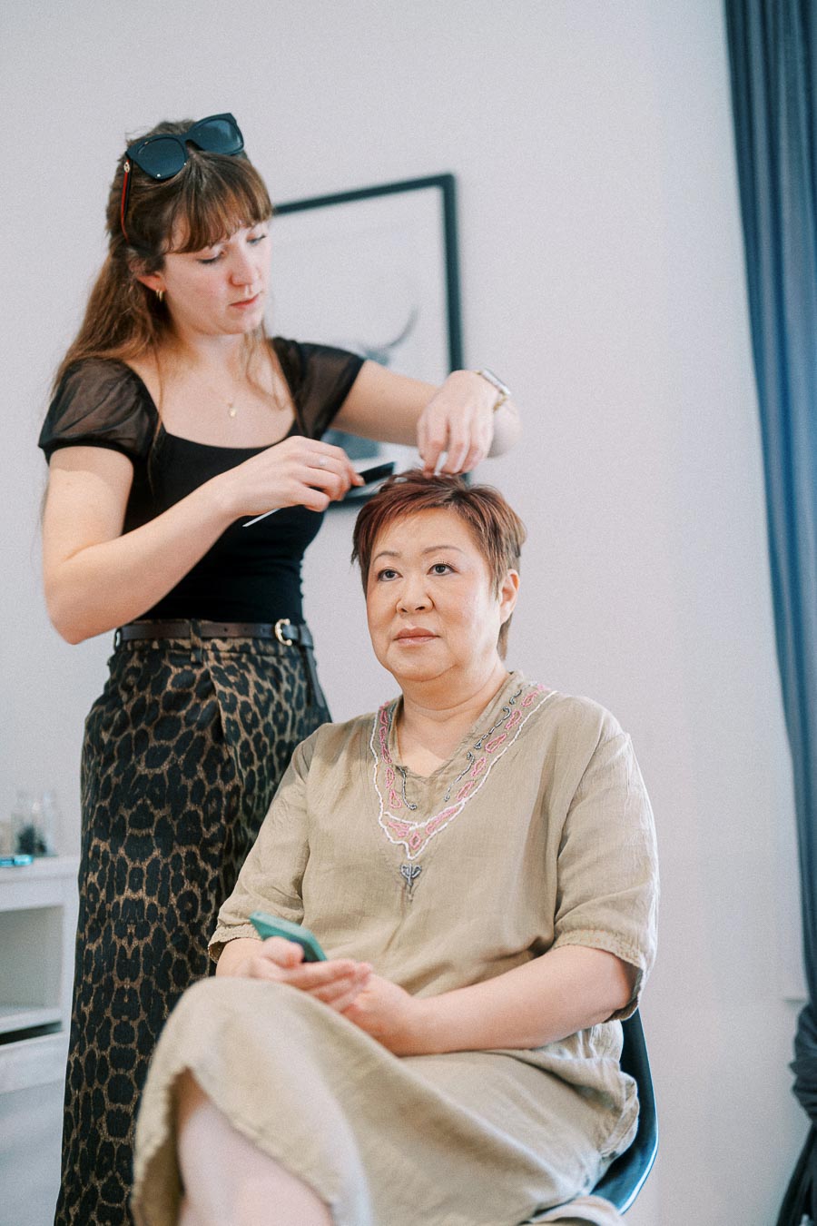 Hairstylist combing a seated woman's short hair during wedding morning preparations indoors