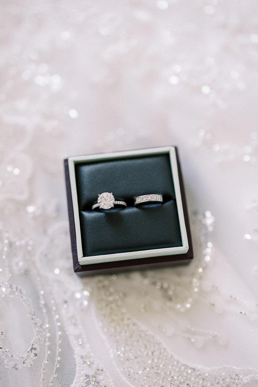 Diamond engagement ring and wedding band in a black ring box on beaded white lace fabric