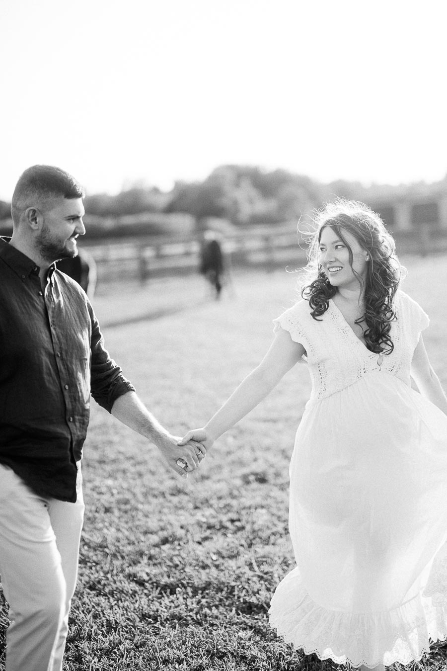 Expectant couple holding hands in a farm field at The Green Acres