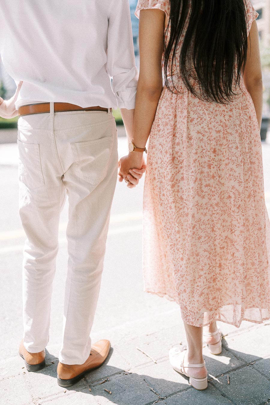 Couple holding hands on a sunlit Toronto sidewalk, seen from behind