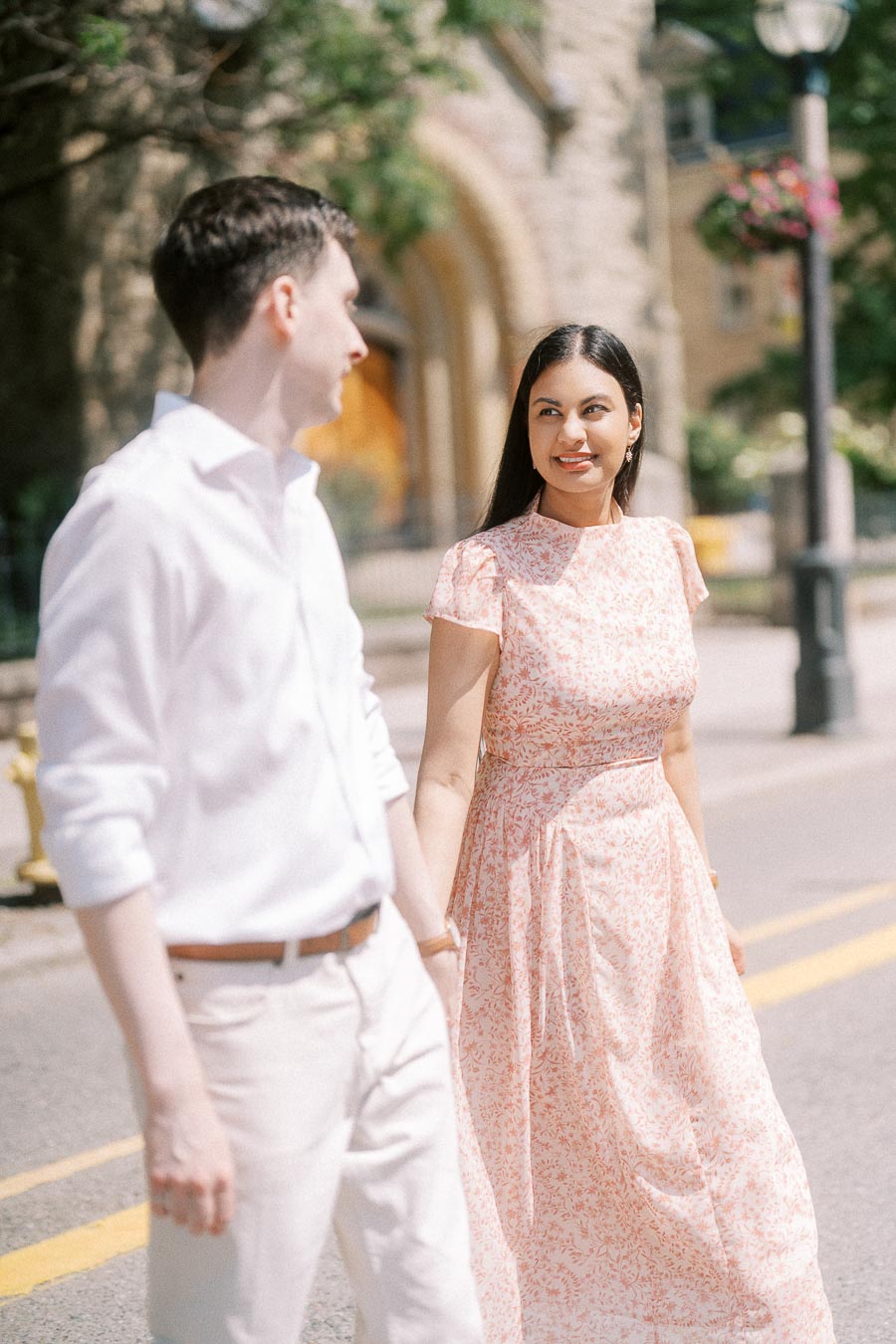 Couple holding hands on a sunny Toronto street beside stone architecture