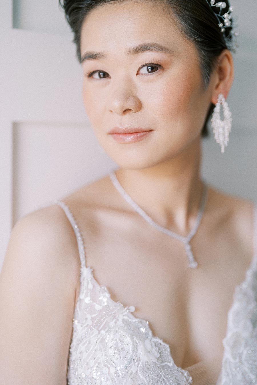 Bride Miffy in a beaded wedding dress with pearl hairpiece, drop earrings, and necklace during getting ready