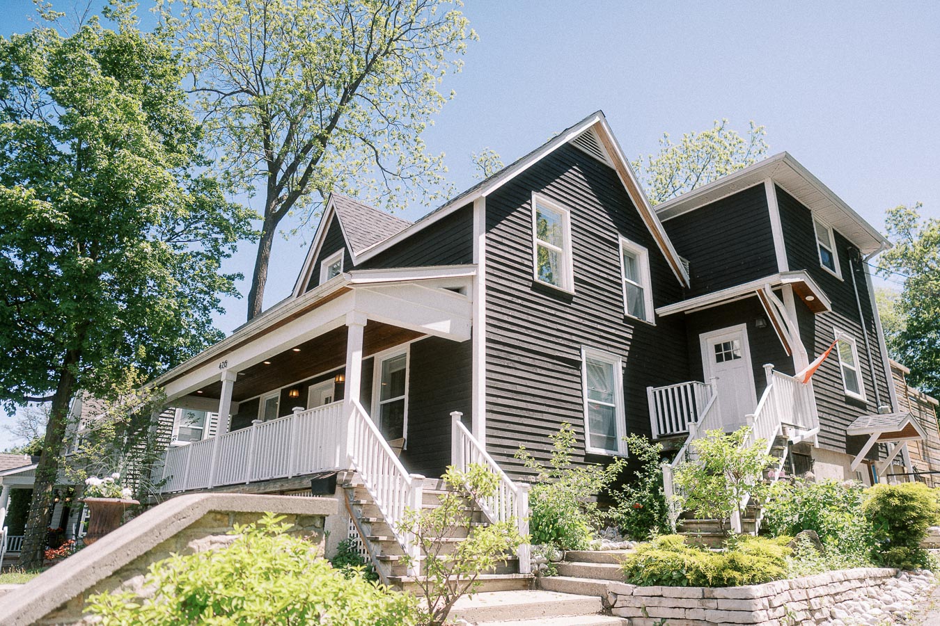 Black house with white porches and garden landscaping under trees on a sunny wedding day in Ancaster.