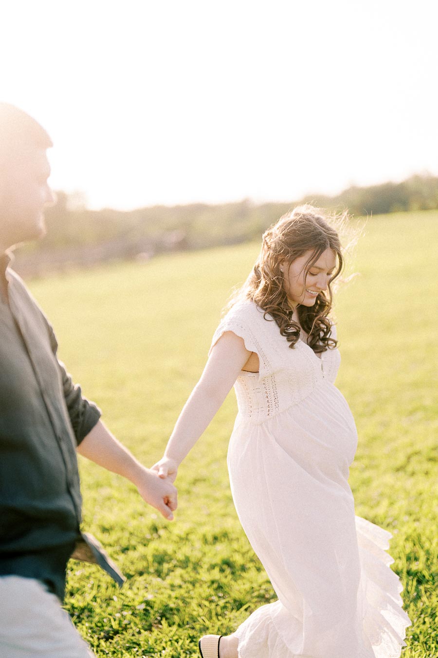 Expectant couple holding hands in a grassy field at The Green Acres