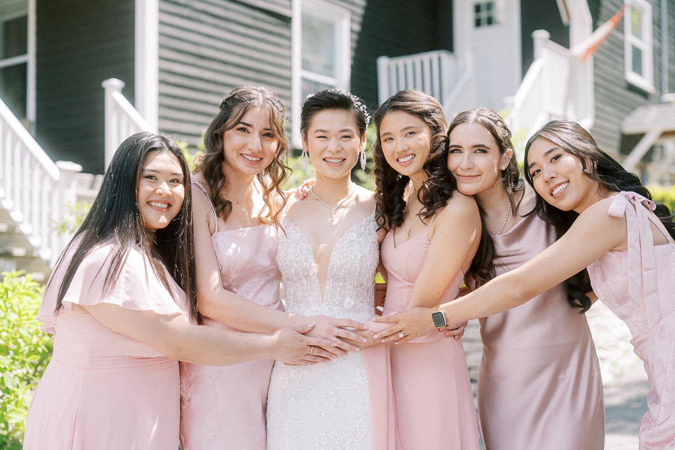 Miffy in a lace wedding dress with five bridesmaids in pale pink dresses smiling outdoors