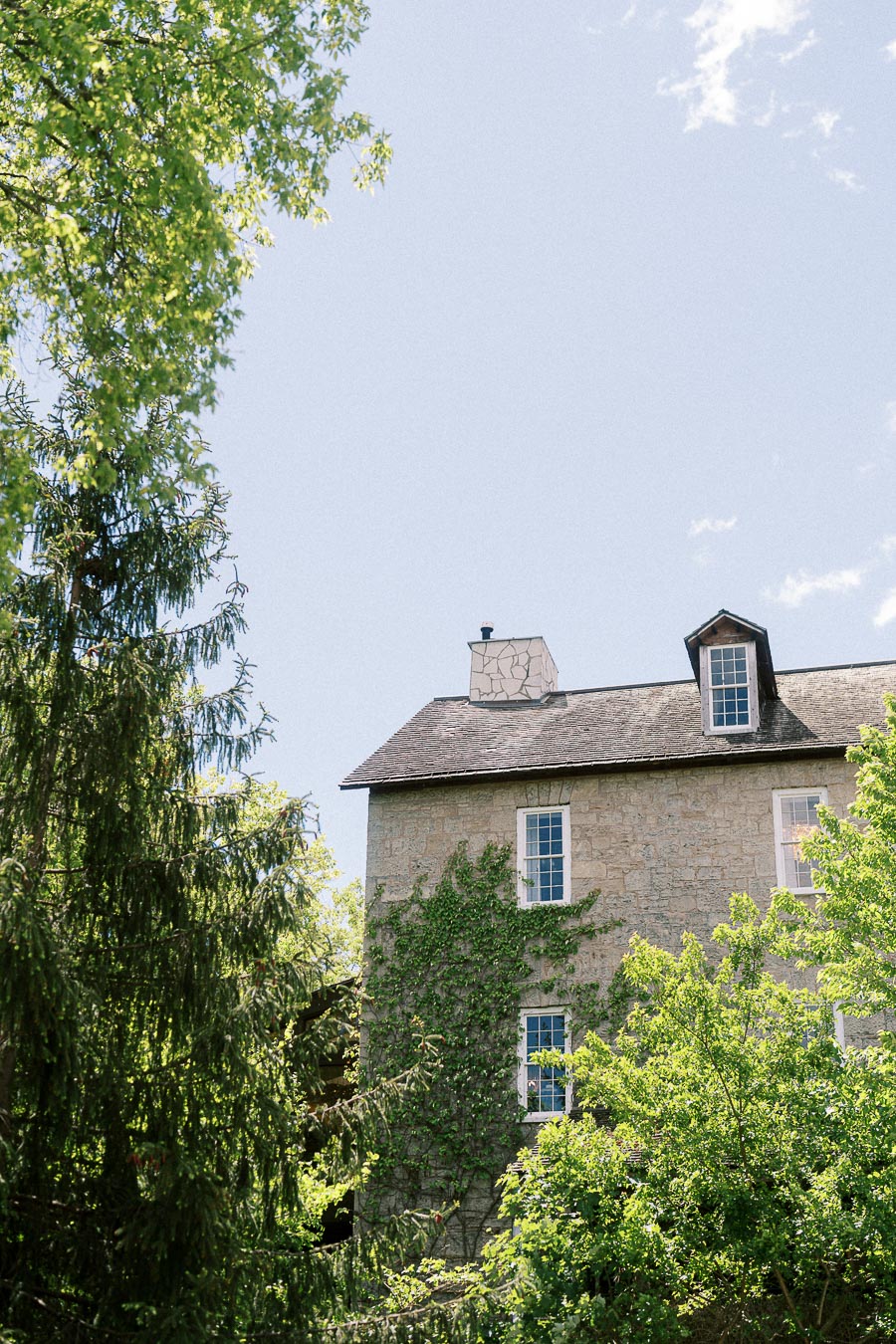 Stone building at Ancaster Mill partly framed by green trees under a bright blue sky