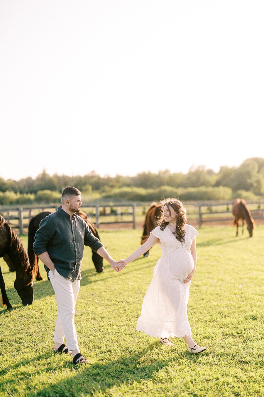 Expectant couple holding hands in a horse pasture at The Green Acres