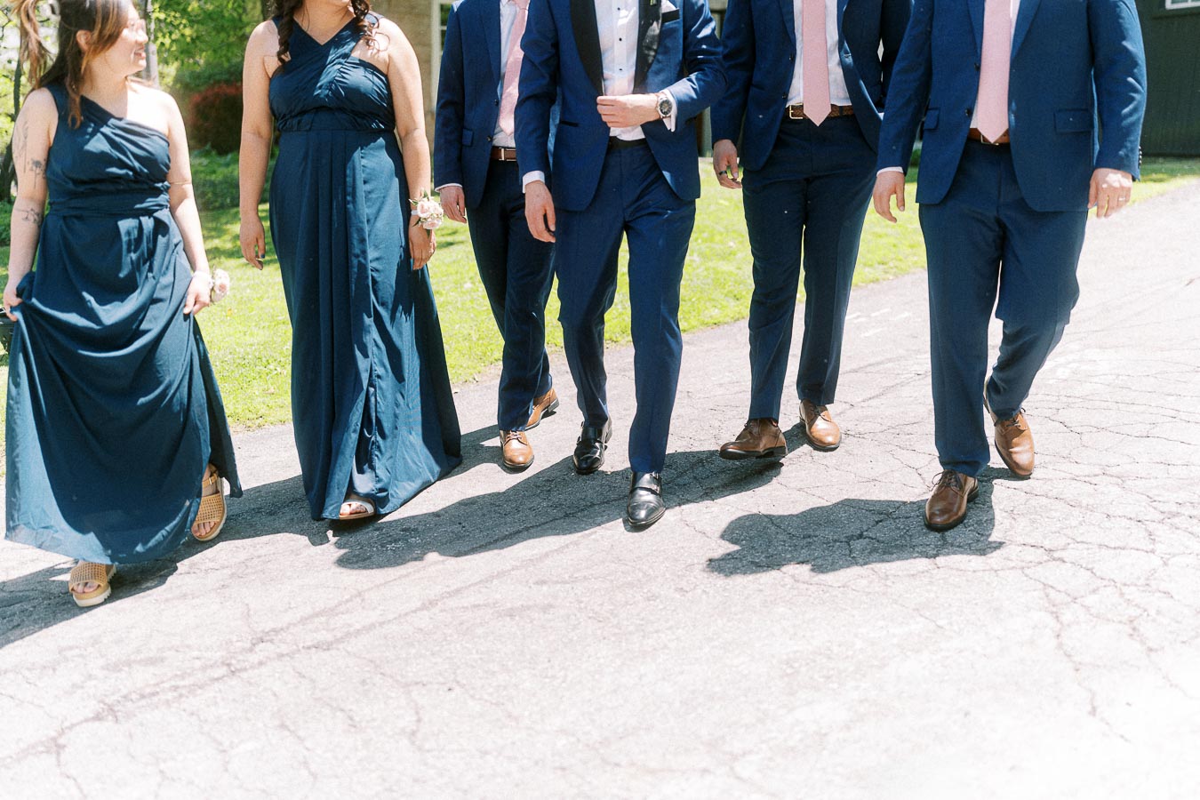 Wedding party members in navy dresses and suits walking together on a sunny paved path