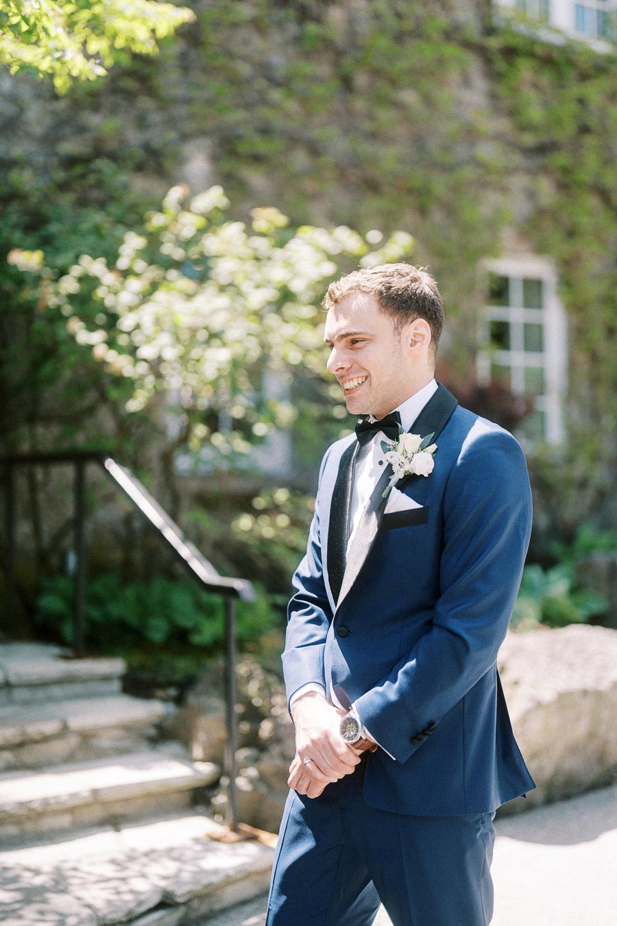 Groom Rawle smiles in a blue tuxedo with boutonniere outdoors at Ancaster Mill.