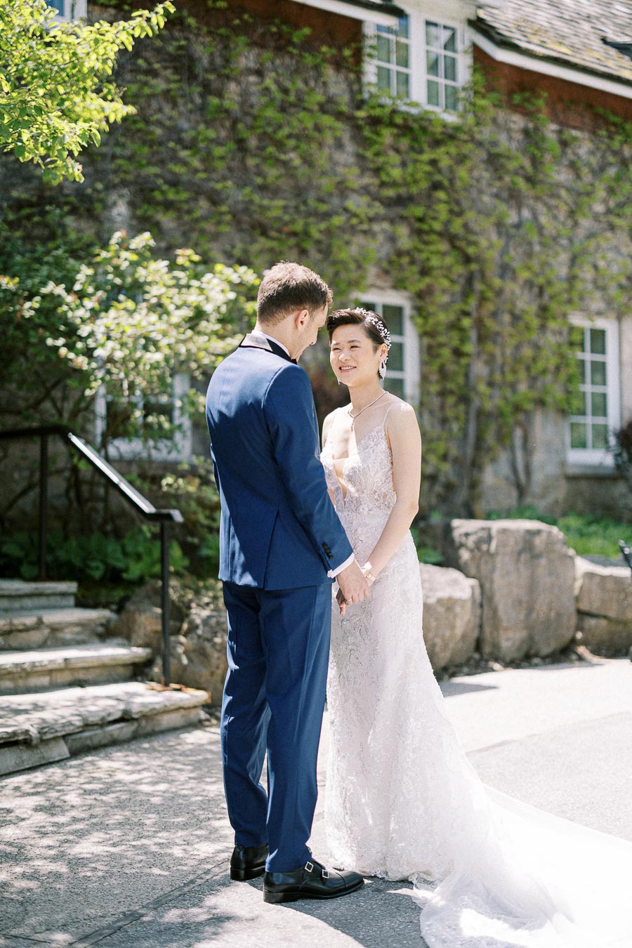 Bride and groom hold hands outdoors in front of a vine-covered stone building at Ancaster Mill.