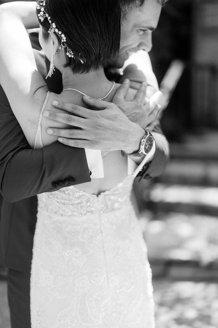 Black-and-white close-up of Miffy and Rawle embracing, showing her beaded gown, hairpiece, earrings, and his watch.