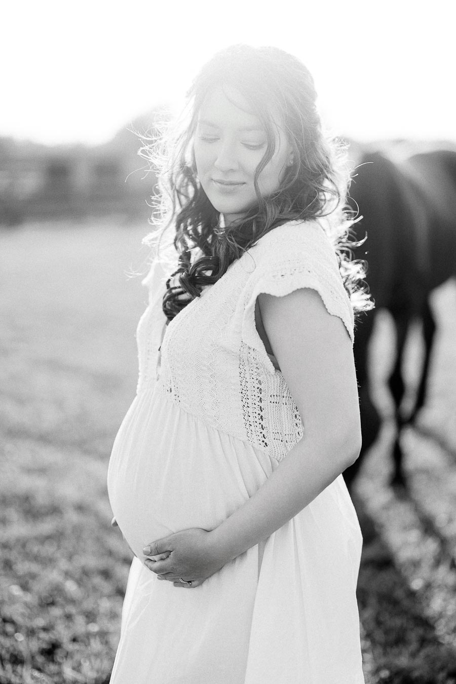 Expectant mother in a white dress with a horse blurred behind her